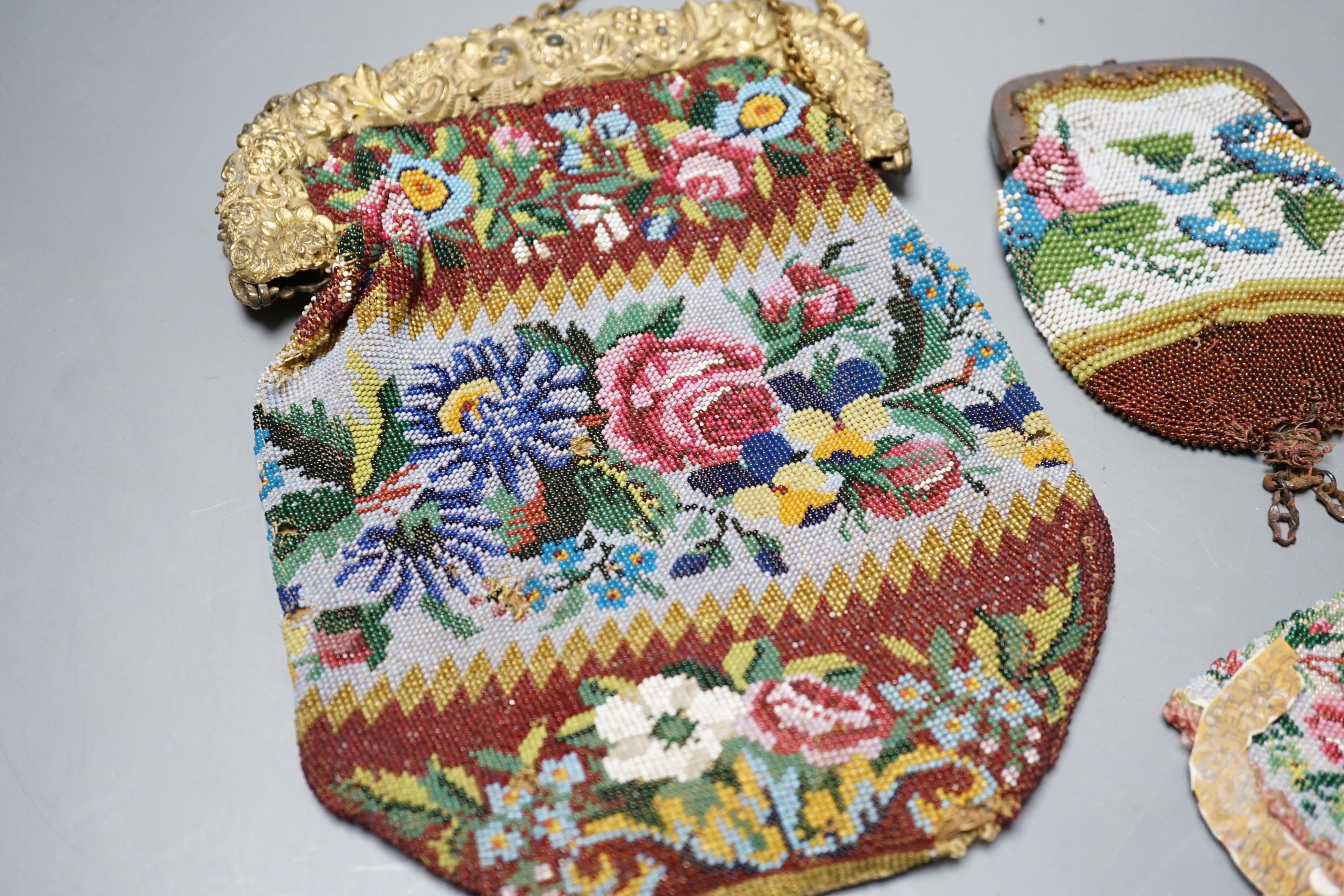 An early 19th century ornate gilt framed beaded bag with multi coloured floral design, together with three similar worked purses, gilt framed bag 20 cms high